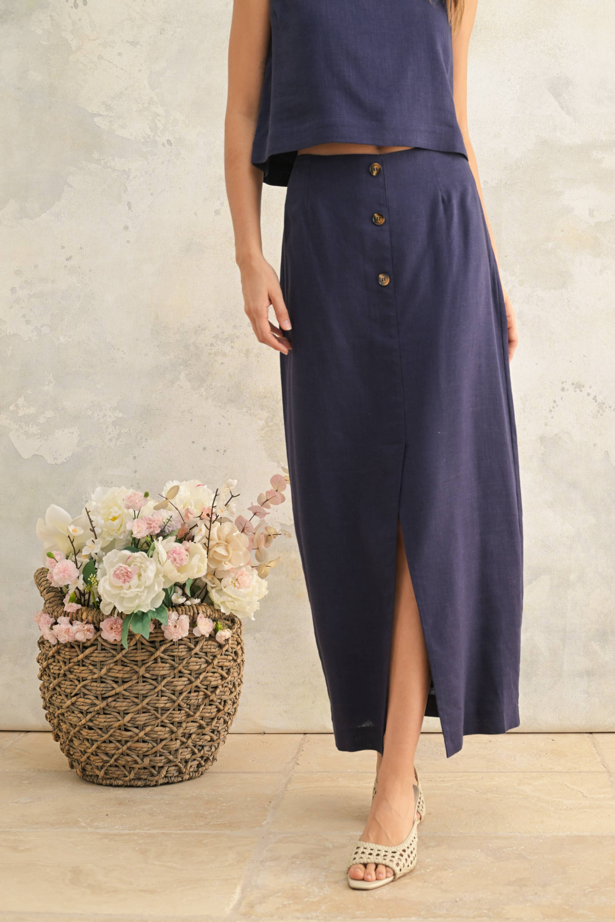 Woman wearing a long navy skirt with a textured wall and flowers in the background