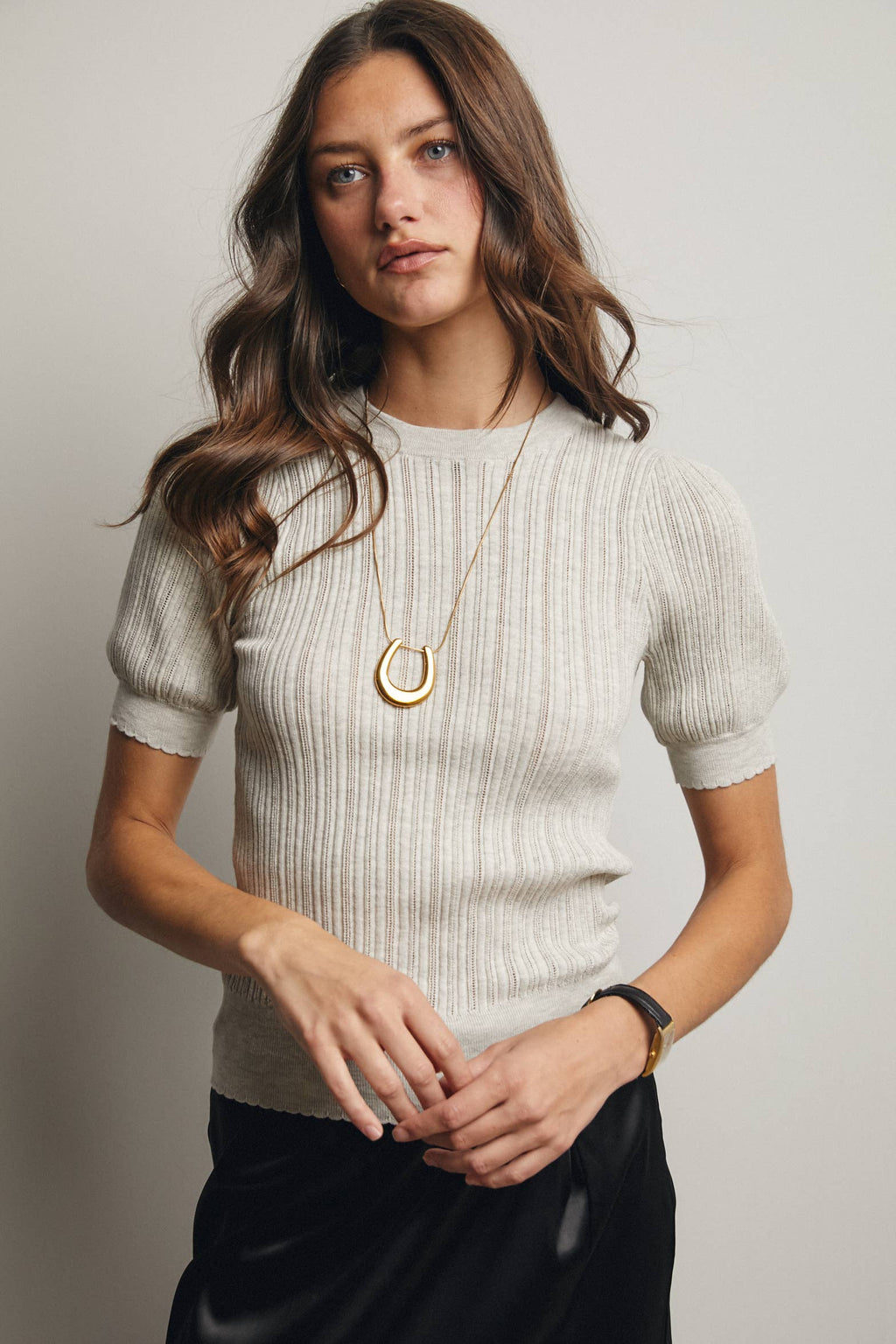 Woman wearing a light-colored sweater and black pants with a plain background