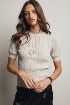 Woman wearing a light-colored sweater and black pants with a plain background